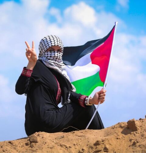 Mujer ondea la bandera de Palestina con signo de victoria.