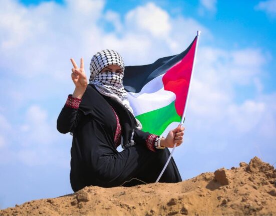 Mujer ondea la bandera de Palestina con signo de victoria.