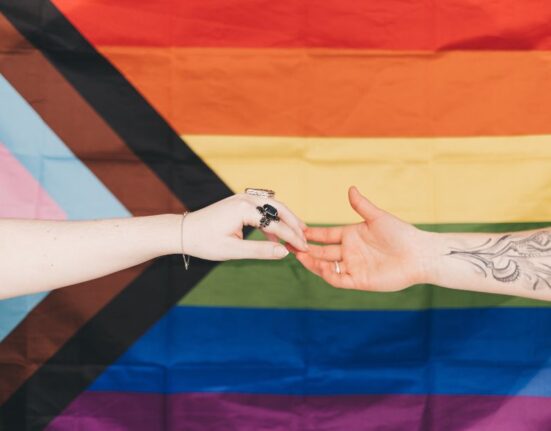 Un hombre y una mujer acercan sus manos sobre una bandera LGBT.