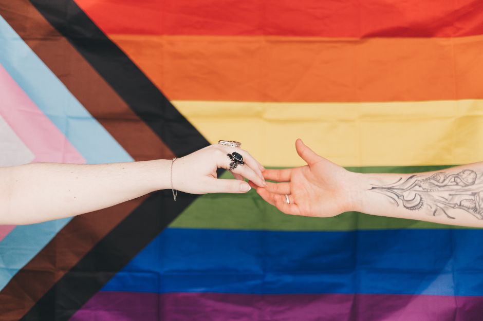Un hombre y una mujer acercan sus manos sobre una bandera LGBT.