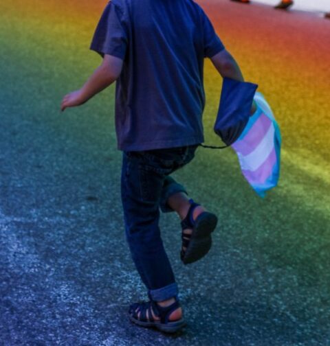 Un niño corre con la bandera trans en la mano.