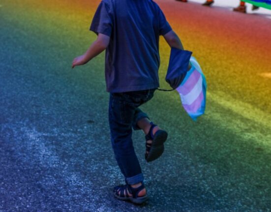 A boy runs with the trans flag in his hand.